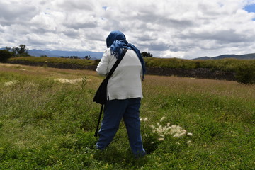 An old woman is looking for wild flowers on a green meadow in Mexico.