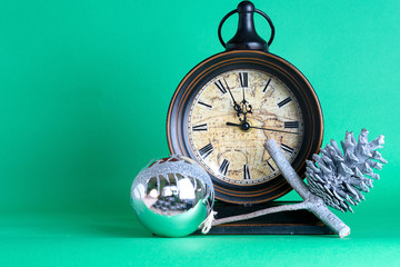 New Year's clock midnight, bauble and cone on pine fir tree branch. Green background. Christmas greeting card.