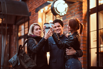Cheerful friends making a toast with coffee near a cafe outside.