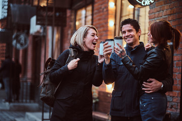 Cheerful friends making a toast with coffee near a cafe outside.