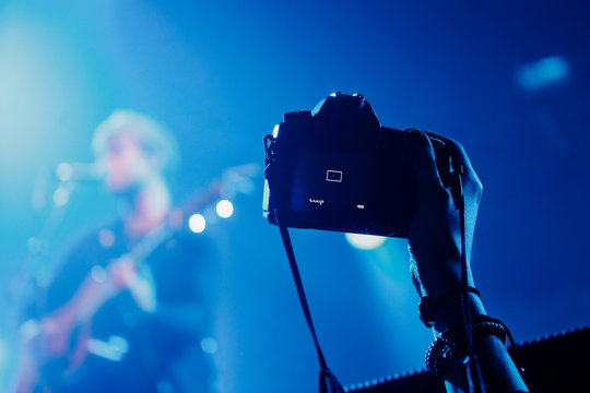 Professional dslr camera at music concert in raised up hand recording singer on a stage