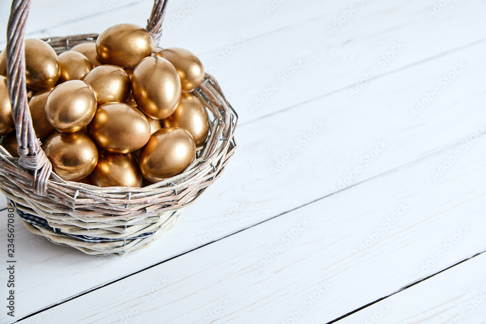 Wall mural golden eggs in the basket on white wooden table background with copy space