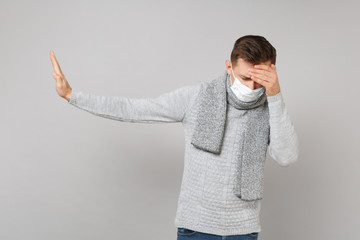Young man in sterile face mask with lowered head putting hands on forehead, showing stop gesture with palm aside isolated on grey background. Healthy, ill sick disease treatment, cold season concept.