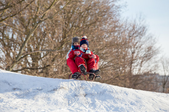 Two boys at the sledge on the top of snowy hill waiting for ridi