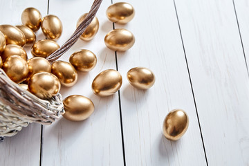 Golden eggs spilled out of wicker basket on white wooden table