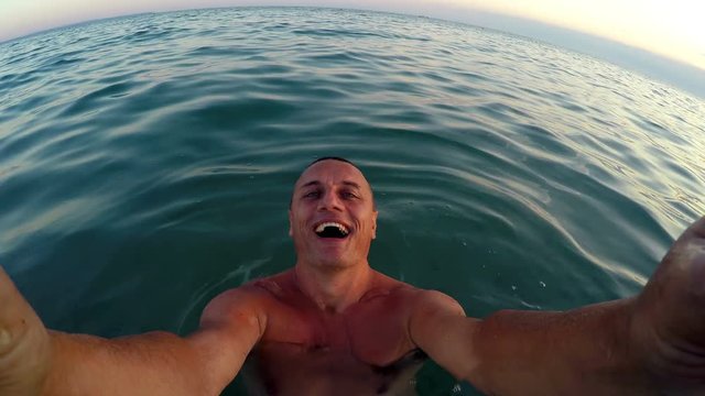 Selfie of handsome man enjoying summer vacation playing and turning in water at sunset