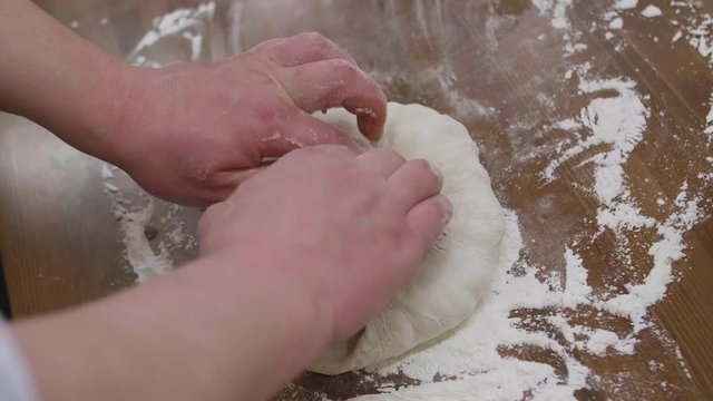 man hands kneading dough on table, making khinkali