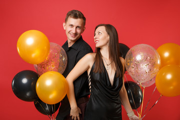 Stunning young couple in black clothes celebrating birthday holiday party isolated on bright red background air balloons. St. Valentine's International Women's Day Happy New Year 2019 concept. Mock up