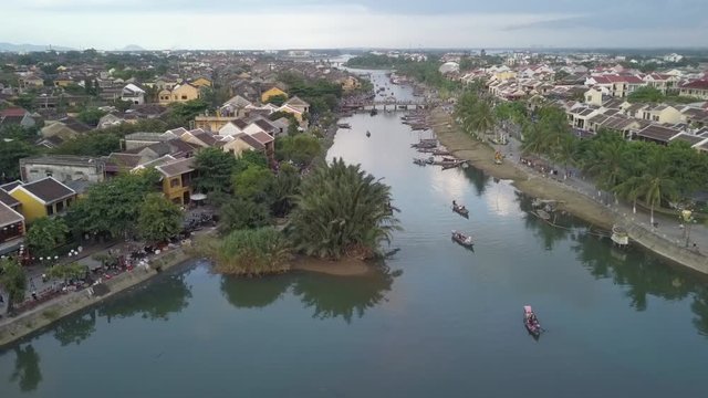 2K Aerial view of the river with some tour boats on water in ancient Hoi An, Vietnam. Hoian city beautiful aerial panorama at sunset