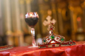 Isolated wedding crown and blurred glass of vine and cross in background. Orthodox church wedding accessories