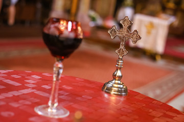 Isolated wedding ceremony cross in background and blurred glass of vine in front. Orthodox church wedding accessories