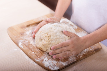 Children's hands knead the dough on a wooden cutting board. close-up. dough recipe, cooking technology