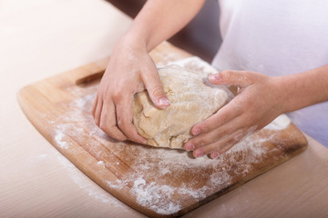 Obraz na płótnie Canvas Children's hands knead the dough on a wooden cutting board. close-up. dough recipe, cooking technology