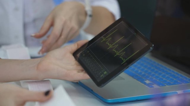 The doctor examines the patient cardiogram on tablet, the nurse writes the advice of a doctor.