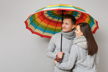 Couple girl guy in gray sweaters scarves together under umbrella isolated on grey wall background,...