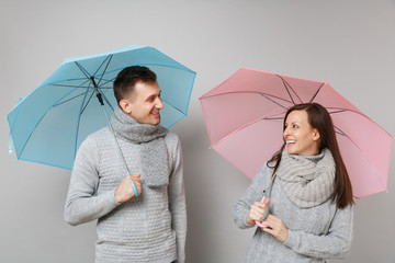 Couple girl guy in gray sweaters scarves together under umbrella isolated on grey wall background,...