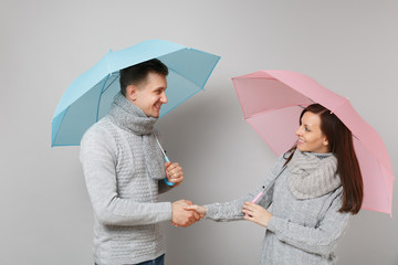 Couple girl guy in gray sweaters scarves together under umbrella isolated on grey wall background,...