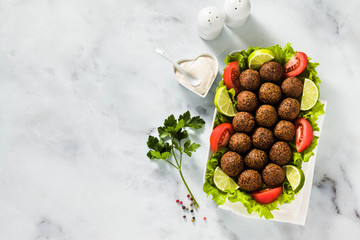 vegan falafel with cashew cheese sauce on a table with chopped tomatoes and lime slices. healthy food for the whole family or party