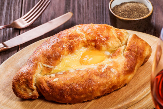 Ajarian Khachapuri traditional Georgian cheese pastry with eggs on cutting board. Homemade baking. Top view