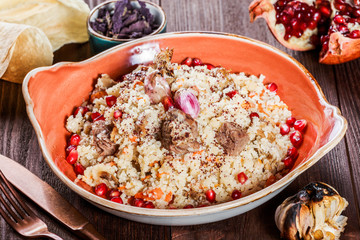 Pilaf with lamb meat, carrots, onions, garlic, pomegranate on plate on wooden background. Traditional dish of Asian cuisine. Top view