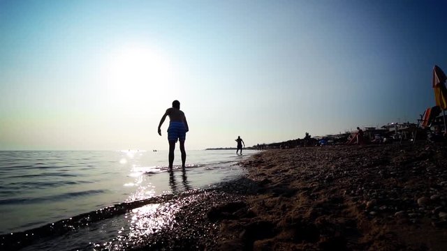 Silhouette people playing with frisbee on the beach backlit by summer sun