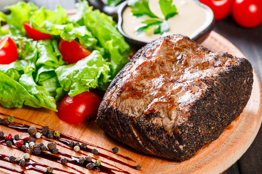 Grilled steak pork with fresh vegetable salad, tomatoes and sauce on wooden cutting board