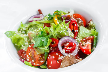 Fresh vegetable salad with lettuce, grilled mushrooms, tomatoes, sweet peppers and sesame seeds on plate on light wooden background close up. Healthy food. Top view