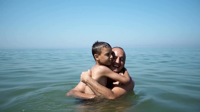 Father and son on beach embracing, smiling and kissing, vacation travel concept