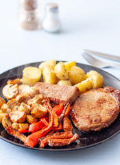 A meal of steak, potatoes, mushrooms and roasted vegetables on a black plate