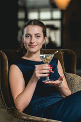 Fashionable gorgeous girl in a dark blue dress drinking cocktail in a luxery hotel lobby bar