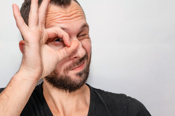 Obraz premium a young guy with a beard looks through his fingers, copyspace