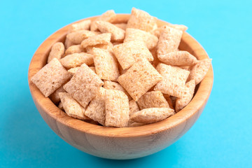 Crunchy corn pads in wooden bowl on bright blue background