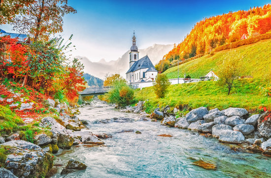 Fantastic Fairytale scenery of Alpine river Ramsauer Ache, mountains Alps, Great view on Parish Church of St. Sebastian in Germany, Bavaria, Europe. Seasonal Autumn Colorful Scene. Countryside scene.