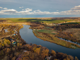 Aerial view of rural landscape in autumn. Small village houses, river, autumn trees, farm fields from drone point of view