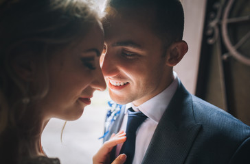 A beautiful toyung bride and a stylish groom stand and hug in the back light. Wedding concept. Wedding portrait of cute and smiling newlyweds.