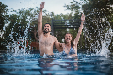 Young couple playing in the outdoor pool. Loving couple splashing water