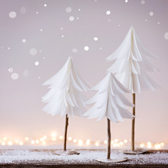Winterliche Weihnachtsdekoration mit kleinen Tannenbäumen aus Papier und Lichterbokeh im...