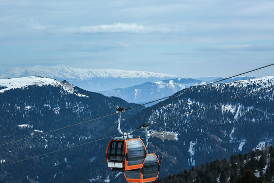 Orange gondola cabins of cableway lift on winter snowy mountains background beautiful scenery