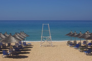 Watchtower of lifeguard inside sunbeds and umbrellas in a sandy beach in a sunny day at Vrachos...
