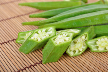 whole and portion cut fresh okras on wooden mat background