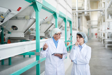 Waist up portrait of senior factory worker walking with trainee across production hall at food factory, copy space