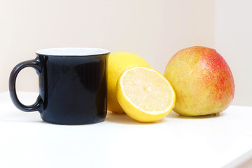 TAZA NEGRA CON MANZANA Y LIMÓN SOBRE ALACENA 