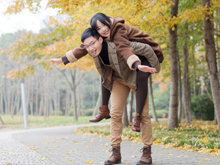 Portrait of smiling young girlfriend piggyback boyfriend during romantic walk in autumn park alley, excited couple looking at camera have fun outdoors, playing foolish, man carry lover on his back.