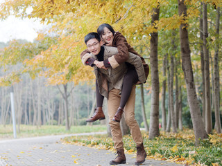 Fototapeta premium Portrait of smiling young girlfriend piggyback boyfriend during romantic walk in autumn park alley, excited couple looking at camera have fun outdoors, playing foolish, man carry lover on his back.
