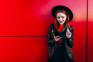 Fashion smiling woman is using smartphone on a red background