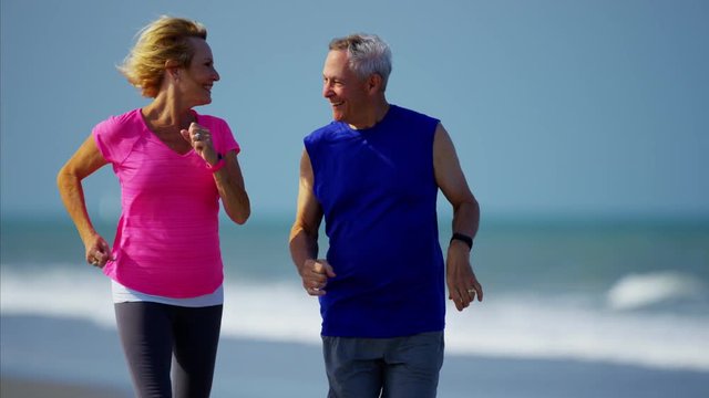 Active retired Caucasian couple enjoying jogging on the beach