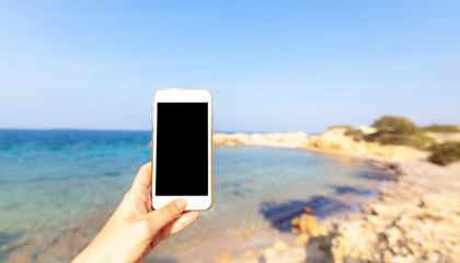 Smartphone mobile phone in female hand on the background of beautiful vivid seascape, technology and travel concept