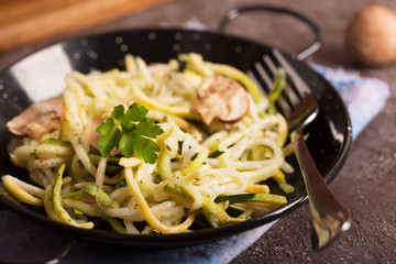 Pan of spaghetti prepared from zucchini and mushroom sauce on wooden table