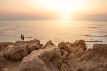 Two people stand along interesting cliffs during ocean sunset © Robert