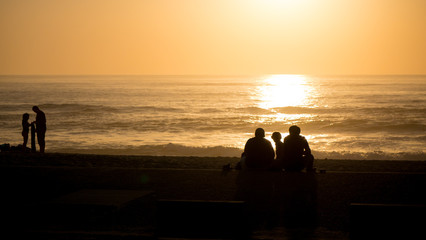 Silhouetted people sit on the beach watching the beautiful sunset in Portugal.